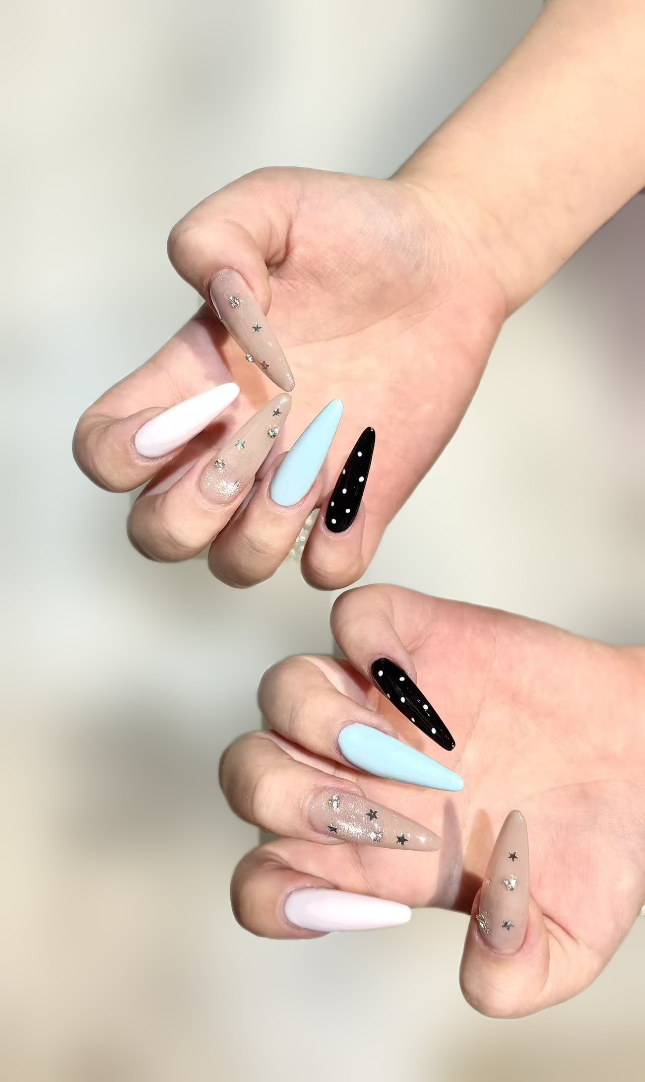 Long stiletto nails in nude with silver stars, pale blue, pale pink, and black with white dots
